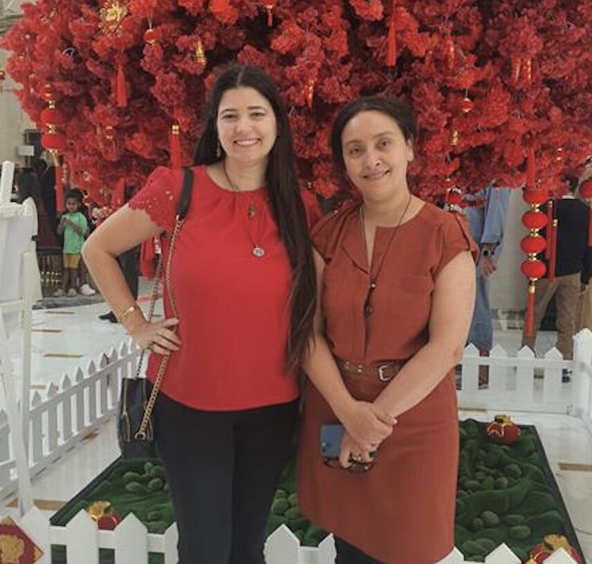 Two women posing in front of red flowers